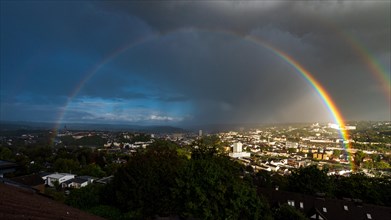 A rainbow stretches over a city with dark clouds and sunny patches, Wuppertal, Bergisches Land,