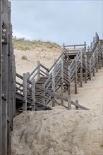 A wooden staircase leads up through sand dunes on an overcast day