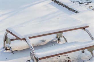 A wooden bench with metal framework covered in a thick layer of snow, in South Korea