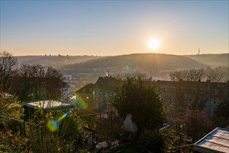 Sunrise over a misty landscape with a view of houses and bare trees in winter, Arrenberg,