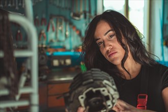 Woman mechanic holding a motorcycle engine part in a workshop, appearing thoughtful, a complete