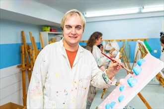 Portrait of a mental disabled man wearing white lab coat smiling at camera in the painting class