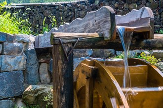 Water pouring onto a wooden water wheel by a stone wall, in South Korea