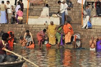 People in traditional dress perform religious rites in river water near stone steps, Varanasi,