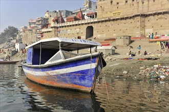 Abandoned boat in the foreground with a view of polluted river ghats, Varanasi, Uttar Pradesh,