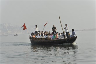 Group of passengers on a boat on a river, with a ferryman steering with a long oar, Varanasi, Uttar
