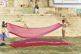 Two people helping to hang colourful laundry on a sunny riverbank, Varanasi, Uttar Pradesh, India,