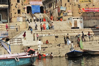 People on the ghats along a river in India with boats in the foreground, Varanasi, Uttar Pradesh,