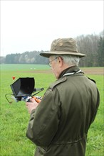 Hunter observes flying drone on the screen of the control unit during a hare (Lepus europaeus)