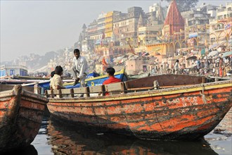 Lively scene on a riverbank with boats and people in front of a city, Varanasi, Uttar Pradesh,