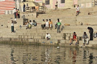 Group of people sitting and interacting by the ghats of a river in an urban environment, Varanasi,