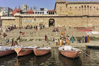 People walking on stairs along a river with docked boats, Varanasi, Uttar Pradesh, India, Asia
