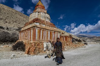 Woman with her horse, colourfully painted Buddhist stupa in front of mountain landscape, erosion