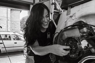 A cheerful female mechanic works on a moped italian vintage scooter motorcycle engine in a