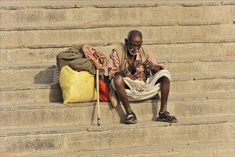 Old man sitting alone on the steps and looking at an object, Varanasi, Uttar Pradesh, India, Asia