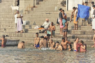 People of different ages bathing in the river and resting on the steps next to it, Varanasi, Uttar