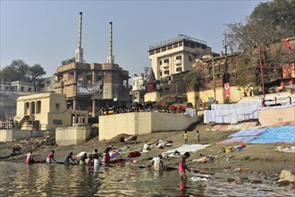 Community washing of clothes on the riverbank with a view of buildings and cultural life, Varanasi,