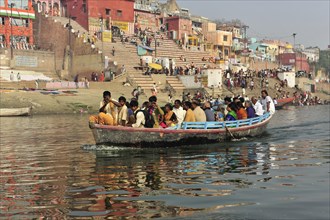 Filled boat with passengers on a river, city in the background, Varanasi, Uttar Pradesh, India,