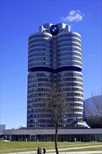 BMW main building, known as the 'four-cylinder', against a clear sky with trees in the foreground,