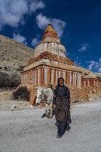 Woman with her horse, colourfully painted Buddhist stupa in front of mountain landscape, erosion
