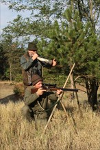 Hunter with rifle at the ready and hunting guide with stag call awaiting red deer (Cervus elaphus)