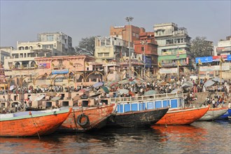 Colourful boats and hustle and bustle on the riverbank against an urban backdrop, Varanasi, Uttar