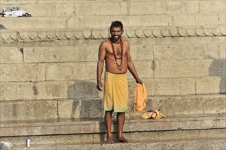 A smiling man in traditional dress stands on the ghats on the riverbank, Varanasi, Uttar Pradesh,
