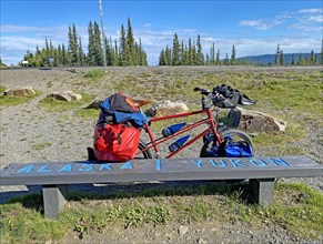 Bench right on the border between Alaska and the Yukon, packed touring bike, adventure travelling,