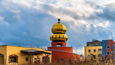 A building with a striking golden dome against a dramatic sky, Hundertwasser Kindergarten,