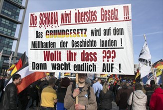A participant in the Merkel muss weg demonstration holds a poster with the inscription Die Scharia