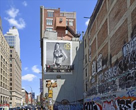 Painter on hanging scaffolding creating mural, advertisement with woman in bikini, graffiti on