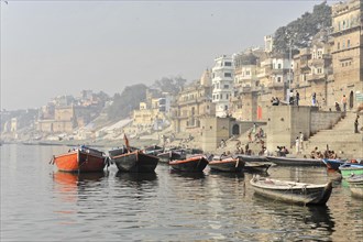 Quiet boats on a misty river against a backdrop of old buildings on the city bank, Varanasi, Uttar