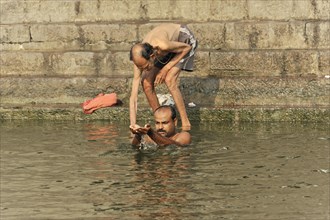 An elderly man helps another man to bathe himself in the river during a traditional ritual,