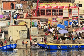 Colourful boats and people on the banks of a river with multi-storey buildings, Varanasi, Uttar