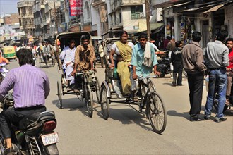 People travelling in cycle rickshaws on a busy street with shops, Varanasi, Uttar Pradesh, India,