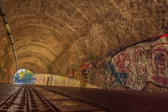 Cycle path through a tunnel with colourful graffiti on the walls and tracks on the floor,