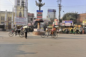 Busy road junction with cyclists and numerous signboards under a clear sky, Varanasi, Uttar
