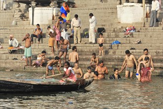 A boat passes a group of people bathing in the water at the river steps, Varanasi, Uttar Pradesh,