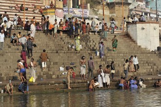 People washing clothes and bathing on the stone steps on the river bank with clear sky, Varanasi,