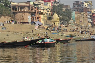 Boats at the edge of a river with people walking along the bank, Varanasi, Uttar Pradesh, India,