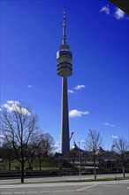 A tall television tower rises into the blue sky with trees in the foreground, BMW WELT, Munich,