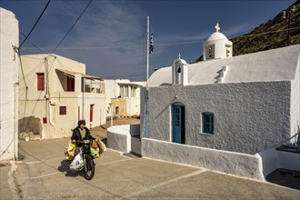 Woman riding a heavily loaded moped in front of Agios Dimitrios Church, Klima, Milos, Cyclades,