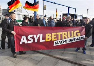 Participants in the Merkel muss weg demonstration hold a sign reading Asylum fraud makes us poor.