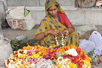 Woman in traditional dress creating handicrafts with flowers at a market, Varanasi, Uttar Pradesh,