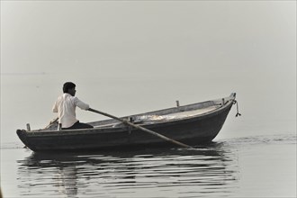 A man rowing alone in a boat on calm water at dawn, Varanasi, Uttar Pradesh, India, Asia