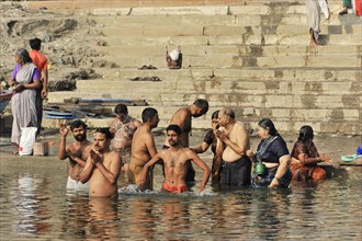 People performing ritual ablutions in the river under the warming morning sun, Varanasi, Uttar
