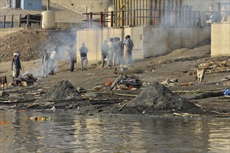 People being cremated near a river, smoke rising and ashes lying on the ground, Varanasi, Uttar