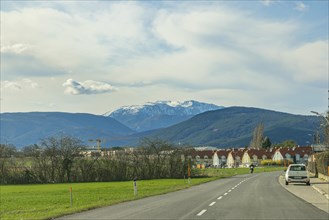 Road leads through a village with a view of the Schneeberg and a cloudy sky, Neunkirchen, Lower