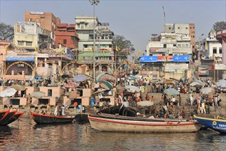 Densely populated shore with people, boats and umbrellas next to water body, Varanasi, Uttar