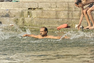 Two men bathing in the river, with water splashes around the swimmer, Varanasi, Uttar Pradesh,